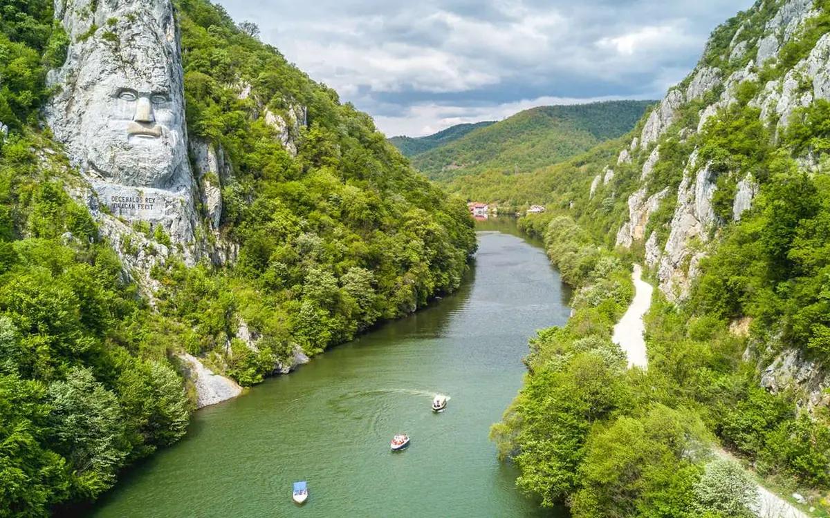Un visage immense sculpté dans la falaise de la rive opposée, avec de petites embarcations sur l'eau
