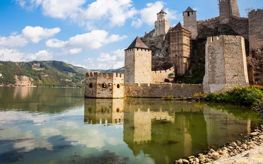 Tours pâles de la forteresse reflétées dans une eau plate sous un ciel bleu parsemé de nuages