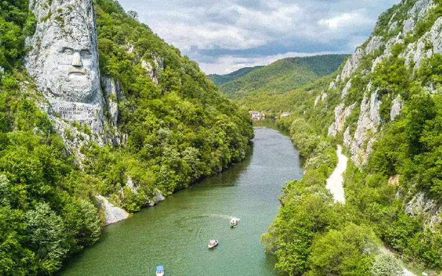Un visage géant sculpté dans la falaise de l&rsquo;autre côté de l&rsquo;eau, avec un petit bateau qui passe en dessous