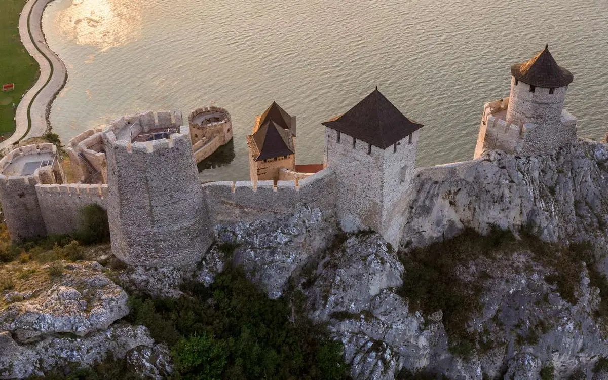 Les tours de la forteresse et son rempart vus d'en haut dans la lumière du soir, le fleuve pâle en arrière-plan