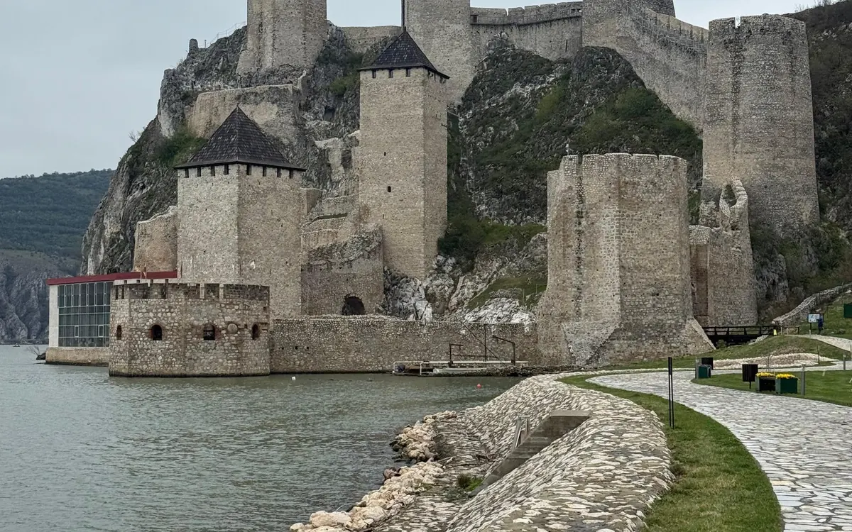 Un chemin pavé au bord du fleuve passant sous les tours de la forteresse de Golubac par temps gris
